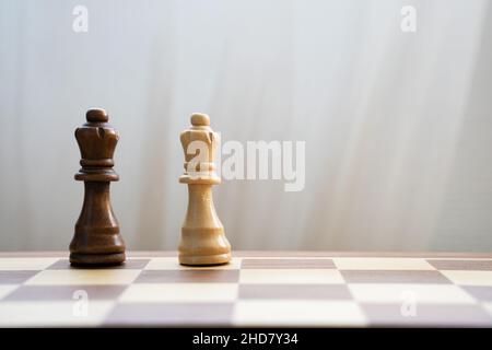 black and white queen pieces on wooden chess board on light background. Interracial relationships and multi-ethnic diversity support concept Stock Photo