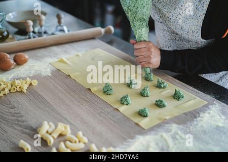 Woman prepare fresh made ravioli inside pasta factory - Focus on hand holding pastry bag Stock Photo