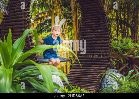 Cute little kid boy with bunny ears having fun with traditional Easter eggs hunt, outdoors. Celebrating Easter holiday. Toddler finding, colorful eggs Stock Photo