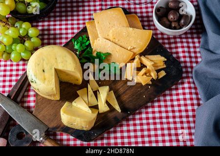 Delicious small spiced cheese piece on a board next to a provolone cheese cut into slices. Aerial view. Stock Photo