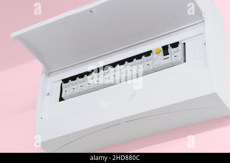 Detail of opened home white fuse box with set of black electric fuses. Pink wall in the back. Electricity and safety. Stock Photo