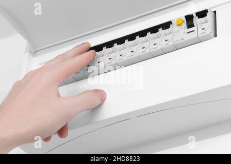 Detail of opened home white fuse box with set of black electric fuses. Male hand in position to switch a fuse off. Electricity and safety. Stock Photo