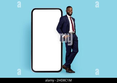 Business App. Handsome Black Male Entrepreneur In Suit Leaning At Blank Smartphone Stock Photo