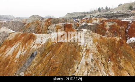 Aerial - Close up of adult male mountaineer in warm clothing hiking on snowy mountain top at beautiful winter sunset. Silhouette of man with trekking Stock Photo