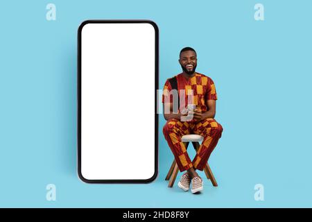 Black Man With Smartphone Sitting On Chair Near Big Blank Phone Stock Photo