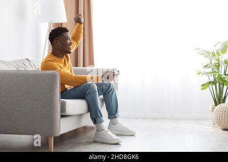 Joyful black guy sitting on couch with joystick Stock Photo