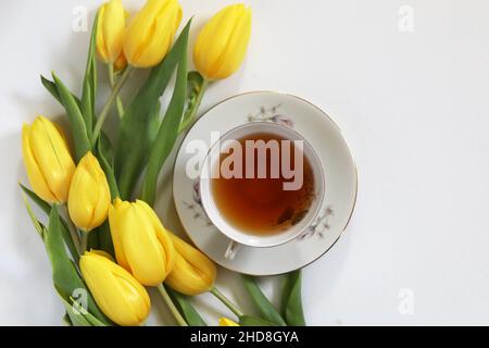 A cup of tea and bunch of yellow tulips on white background. Concept of holiday, birthday, Easter, March 8.  Stock Photo