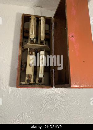 Old ceramic fuse box with exposed fuses mounted on a white wall showing vintage electrical switches and fuses Northampton UK installation equipment Stock Photo