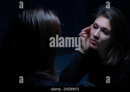 A young adult woman looking at her face throughout the mirror before the makeup Stock Photo