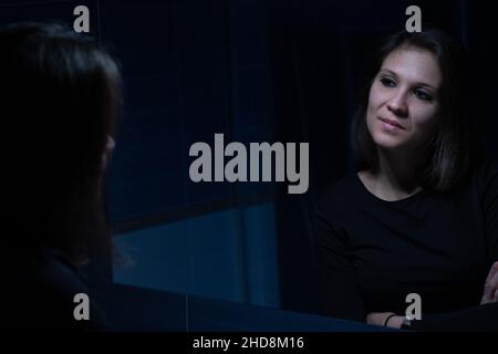 A young adult woman looking at her face throughout the mirror before the makeup Stock Photo