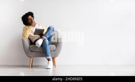 Portrait Of Pensive African American Guy Sitting In Chair With Digital Tablet Stock Photo