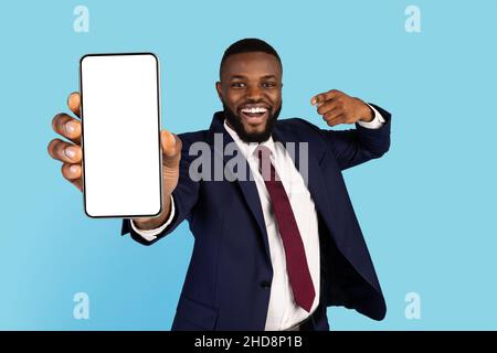 Handsome Black Businessman In Suit Pointing At Big Blank Smartphone In Hand Stock Photo