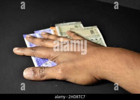 A close up Shot of a man grabbing Indian currency Notes against a black Background Stock Photo