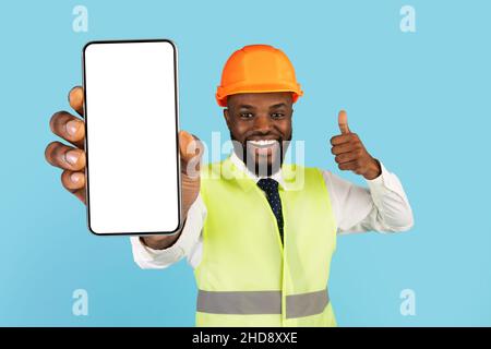 Building Services. Black Construction Worker Demonstrating Blank Smartphone And Showing Thumb Up Stock Photo