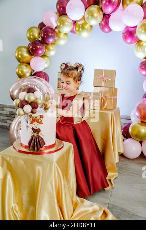 Fashionable two year old little girl standing behind her birthday cake and playing, trying to cut. Lovely baby girl birthday photoshoot Stock Photo