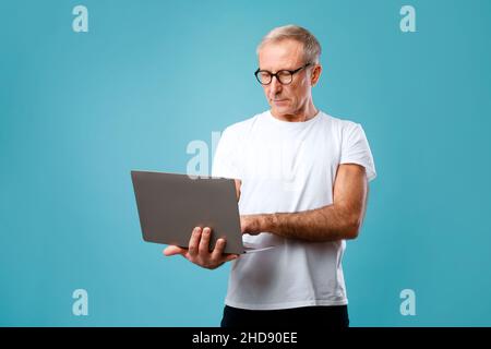 Confident mature man in eyeglasses holding and using laptop Stock Photo