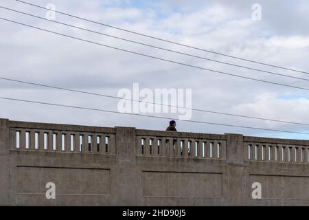 Cambridge, Ontario, Canada - October 23 2021: Elderly man in blue turban and surgical mask walking across stone bridge. Hydro lines overhead. Stock Photo