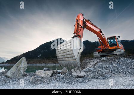 heavy organge excavator with shovel standing on hill with rocks Stock Photo