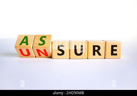 Assure or unsure symbol. Turned wooden cubes and changed the concept word unsure to assure. Beautiful white table, white background, copy space. Busin Stock Photo