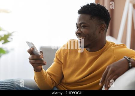Happy black guy chatting with girlfriend, using cellphone at home Stock Photo