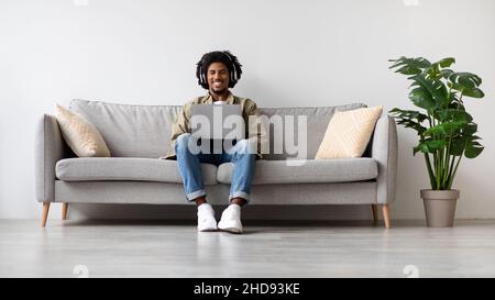 Happy African American Guy Wearing Wireless Headphones Relaxing With Laptop At Home Stock Photo