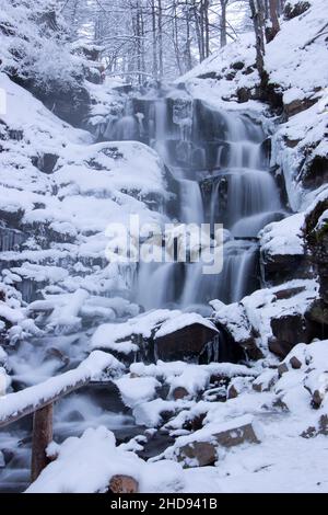 The waterfall is covered with snow. Winter landscape by the river Stock Photo