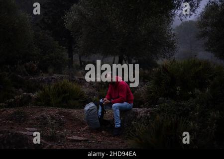 Hiker with red sweatshirt sitting on a stone in the forest on a foggy day Stock Photo