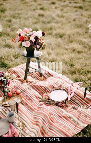 Bouquet of flowers in a flowerpot stands on a small stool on a colorful bedspread in the field Stock Photo