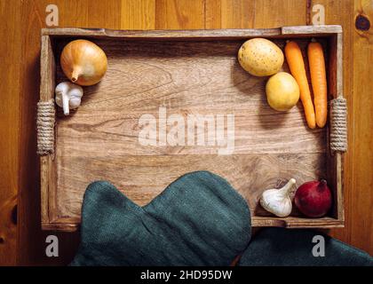 Flat lay view of various root vegetables on wooden tray on kitchen table. Lot of copy space in the center. Carrots, garlic, onion, potatoes. Stock Photo