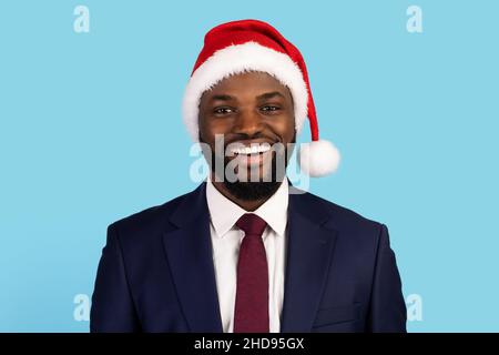 Smiling african american businessman in santa hat posing over blue background Stock Photo
