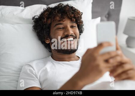 Cheerful young indian man chatting with girlfriend in bed Stock Photo