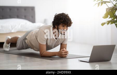 Happy athletic hindu man planking at home, using computer Stock Photo