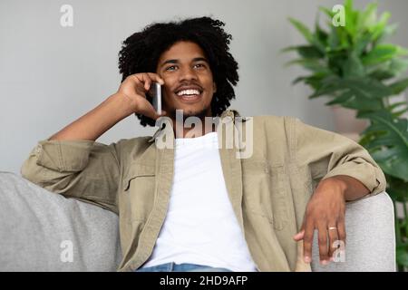 Pleasant Call. Happy Smiling African American Man Talking On Cellphone At Home Stock Photo