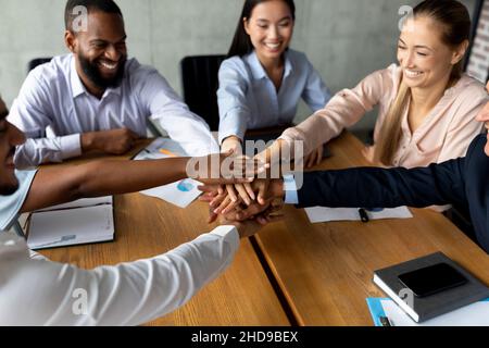 Teambuilding Concept. Happy Multiethnic Coworkers Stacking Hands Together During Meeting In Office Stock Photo
