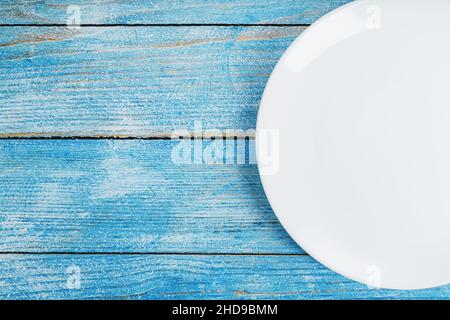 An empty round white plate on a blue wooden table. Top view Stock Photo