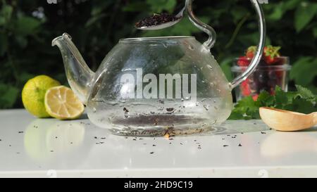 Pouring tea from a teapot into a cup on a blurred background of nature. nearby is lemon and lemongrass, wild berries. pour boiling water into a kettle Stock Photo