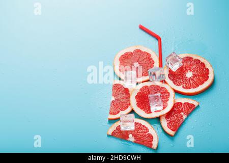 A composition of grapefruit slices and ice cubes with a straw on a blue background in the form of a refreshing drink. Top view, free space Stock Photo