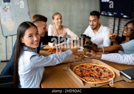 Office Party. Multiethnic Group Of Colleagues Drinking Coffee And Eating Pizza Together Stock Photo