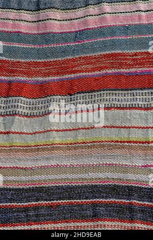 striped woven fabric with multi-coloured design for use as rug or mat, handmade weaving on a rainbow coloured woven floor covering. Stock Photo