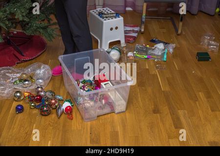 Close up view of woman's feet near plastic box with Christmas tree decoration toys. Undecorating of Christmas tree. Sweden. Stock Photo