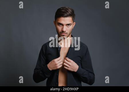 Portrait of unshaven young man buttoning up black shirt Stock Photo