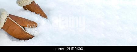 Woman in leather mittens rolls a snowball outdoors, close-up. Hands in warm mittens make snow in winter. Brown leather mittens in the snow in winter. Stock Photo