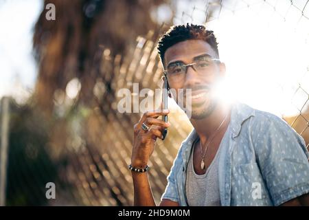 Portrait of handsome afro man using his smartphone smiling on the street looking at camera Stock Photo