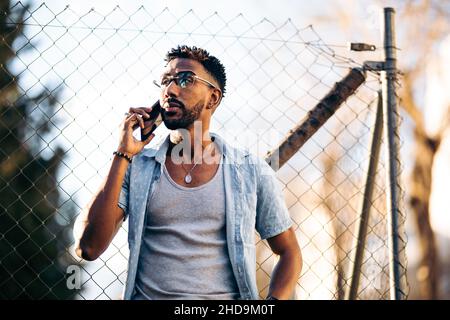 Handsome afro man using his smartphone in the neighborhood leaning on a fence Stock Photo