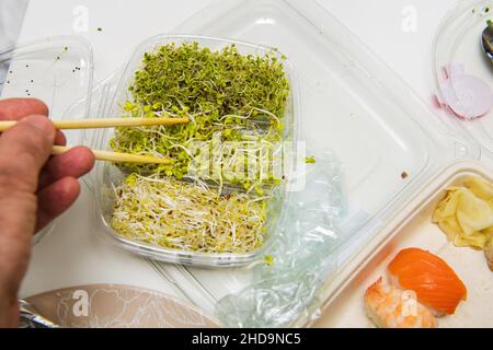 male eating with chopsticks organic broccoli arugula sprouts from the plastic box with multiple sushi Stock Photo