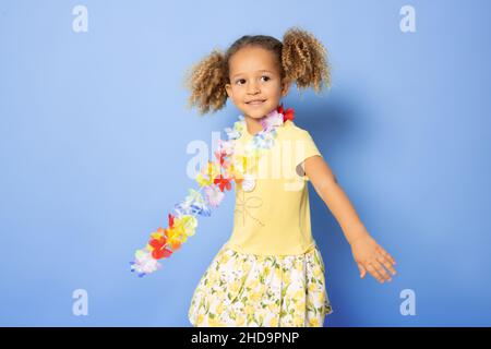 Happy little girl wearing Hawaiian necklace standing isolated over purple background. Stock Photo