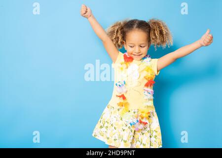 Happy little girl wearing Hawaiian necklace standing isolated over blue background. Stock Photo