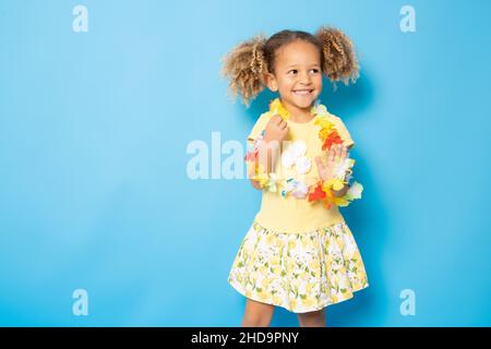 Happy little girl wearing Hawaiian necklace standing isolated over blue background. Stock Photo