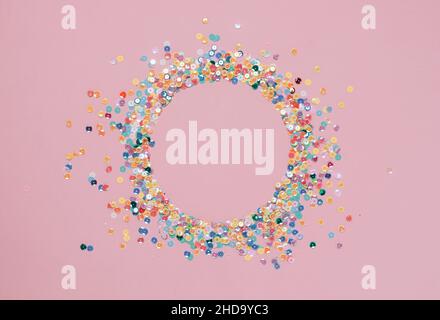 Sequins multicolored confetti lined in round frame pink background. Abstract festive composition place for text Stock Photo