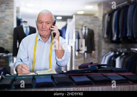 Professional tailor man talking on mobile phone and making notes in notebook Stock Photo